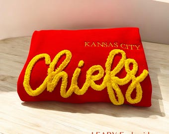 May include: Red sweatshirt with "Kansas City Chiefs" embroidered in yellow fluffy lettering. The text "LEARY Embroidery" is printed in black below the embroidery.