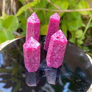 May include: Four pink, rough-textured, pointed crystal shapes on a black surface. The crystals are all about the same size and shape.