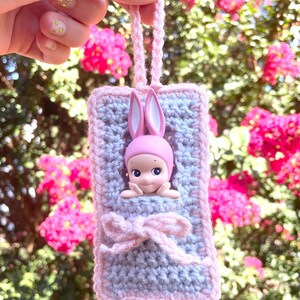 May include: A crocheted gray and pink pouch with a pink bunny doll inside. The pouch has a pink ribbon and a loop for hanging.