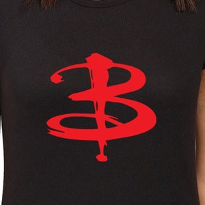 Pode incluir: Camiseta preta com um símbolo "B" estilizado em vermelho na frente. O símbolo é um design popular do programa de televisão "Buffy, a Caça-Vampiros".