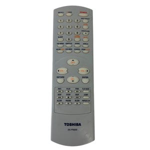 Puede incluir: Un mando a distancia gris Toshiba DC-FN20S con numerosos botones para funciones de TV. Incluye controles de encendido, volumen, canal y teclas numéricas. El mando tiene forma rectangular.