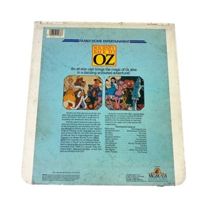 Puede incluir: Una car&aacute;tula de cinta VHS vintage para la pel&iacute;cula animada "El Mago de Oz: El Regreso". La car&aacute;tula presenta una ilustraci&oacute;n colorida de Dorothy, Toto, el Le&oacute;n Cobarde, el Espantap&aacute;jaros y el Hombre de Hojalata. El texto "El Mago de Oz: El Regreso" est&aacute; en una fuente grande y en negrita. La car&aacute;tula tambi&eacute;n incluye una lista de los actores de voz y una descripci&oacute;n de la pel&iacute;cula.