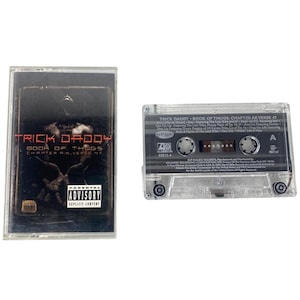 May include: A clear cassette tape and case featuring the album "Book of Thugs Chapter AK Verse 47" by Trick Daddy. The album cover is dark with red text and a parental advisory warning.