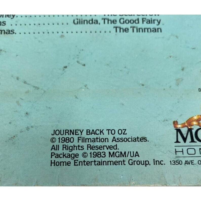 Puede incluir: Una caja de cinta VHS azul con el t&iacute;tulo "Journey Back to Oz" e informaci&oacute;n de copyright para Filmation Associates y MGM/UA Home Entertainment Group, Inc. La caja presenta un dise&ntilde;o de tira de pel&iacute;cula con el logotipo de MGM.