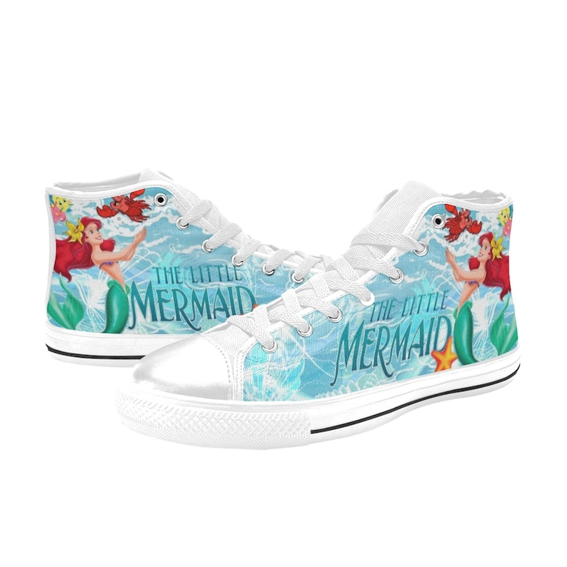 May include: White high-top sneakers featuring a design from "The Little Mermaid." The shoes display Ariel, Flounder, and Sebastian against a light blue background with the movie title. The sneakers have white laces and soles.