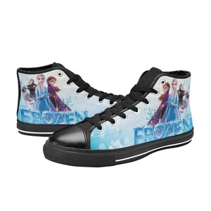 Puede incluir: Zapatillas de lona negras de ca&ntilde;a alta con tem&aacute;tica de Frozen. Las zapatillas tienen un fondo azul y blanco con im&aacute;genes de Elsa, Anna, Olaf y Kristoff. El texto "Frozen" est&aacute; impreso en las zapatillas.