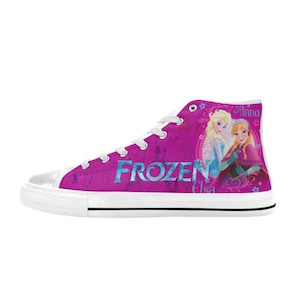 May include: White high-top canvas shoes with a pink background featuring a graphic of Elsa and Anna from the movie Frozen. The text "FROZEN" is printed in blue on the shoes.