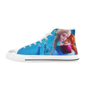 Puede incluir: Zapatillas blancas de lona de ca&ntilde;a alta con un fondo azul que representa una escena de la pel&iacute;cula Frozen. La imagen muestra a Elsa y Anna abraz&aacute;ndose, con Olaf y Sven en el fondo.