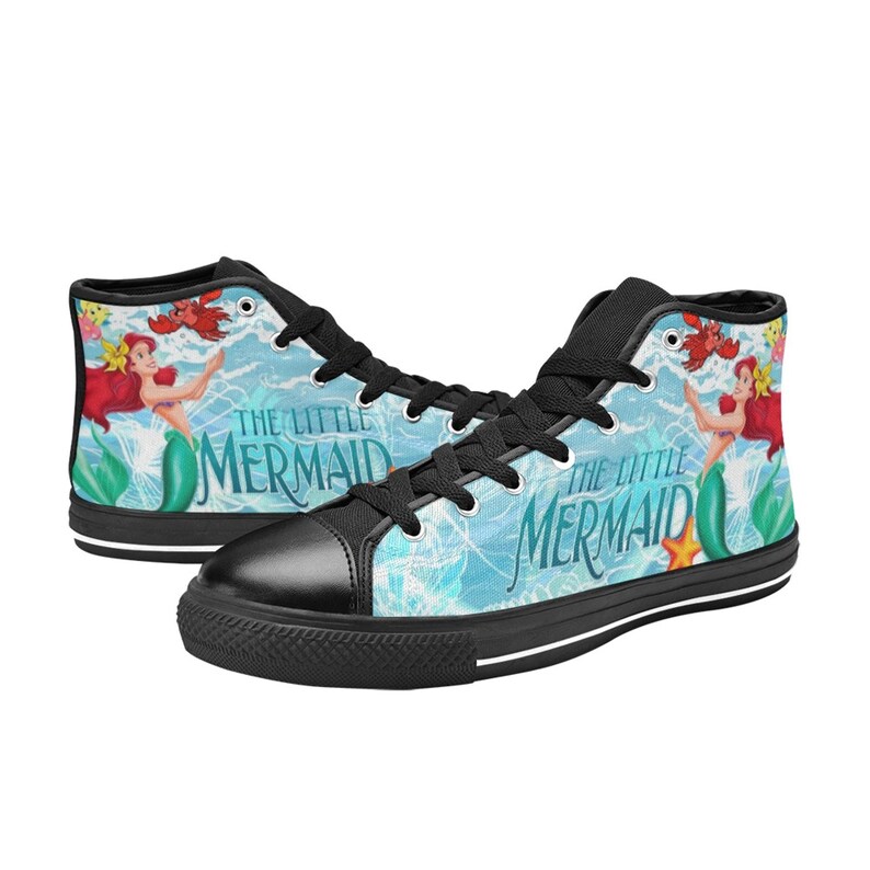 May include: High-top canvas sneakers featuring a design from "The Little Mermaid." The shoes have a black toe cap, laces, and soles. The sides display Ariel, Flounder, and Sebastian against a light blue background with the movie title.