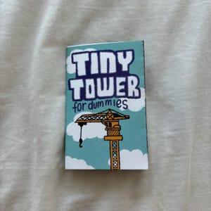 Puede incluir: Un libro azul y blanco con el título "Tiny Tower for dummies" en letras azules en negrita. La portada presenta una ilustración de dibujos animados de una grúa de construcción amarilla contra un cielo azul con nubes blancas.