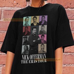 May include: Black t-shirt with a collage of images of Nick Offerman in different styles. The text "NICK OFFERMAN THE ERAS TOUR" is printed in white below the images. The shirt is worn by a person.