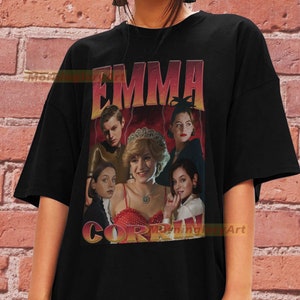 May include: Black t-shirt with a graphic print of Emma Corrin as Princess Diana. The graphic features a collage of images of Corrin in different roles, including as Diana, as a young woman, and as a queen. The text "EMMA CORRIN" is printed in large, bold letters across the top of the graphic.