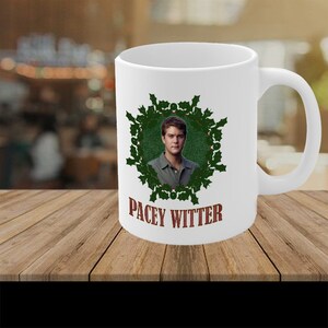 May include: White ceramic coffee mug with a green holly wreath design and a photo of a man inside the wreath. The text "Pacey Witter" is printed in brown below the wreath.