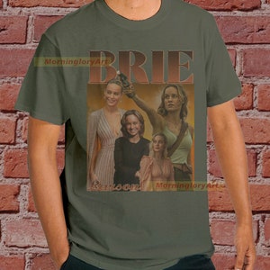 May include: A green t-shirt with a vintage-style graphic of Brie Larson. The graphic features multiple images of Brie Larson in different poses, with the word "BRIE" in large, bold letters above the images.