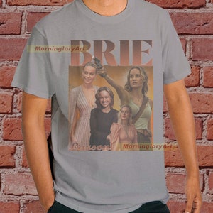 May include: A gray t-shirt with a collage of images of Brie Larson. The text "BRIE LARSON" is printed on the shirt in a retro style.