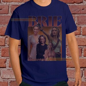 May include: A navy blue t-shirt with a collage of images of Brie Larson. The images are in a retro style with a red and orange color scheme. The text "BRIE" is printed in large, bold letters above the images.