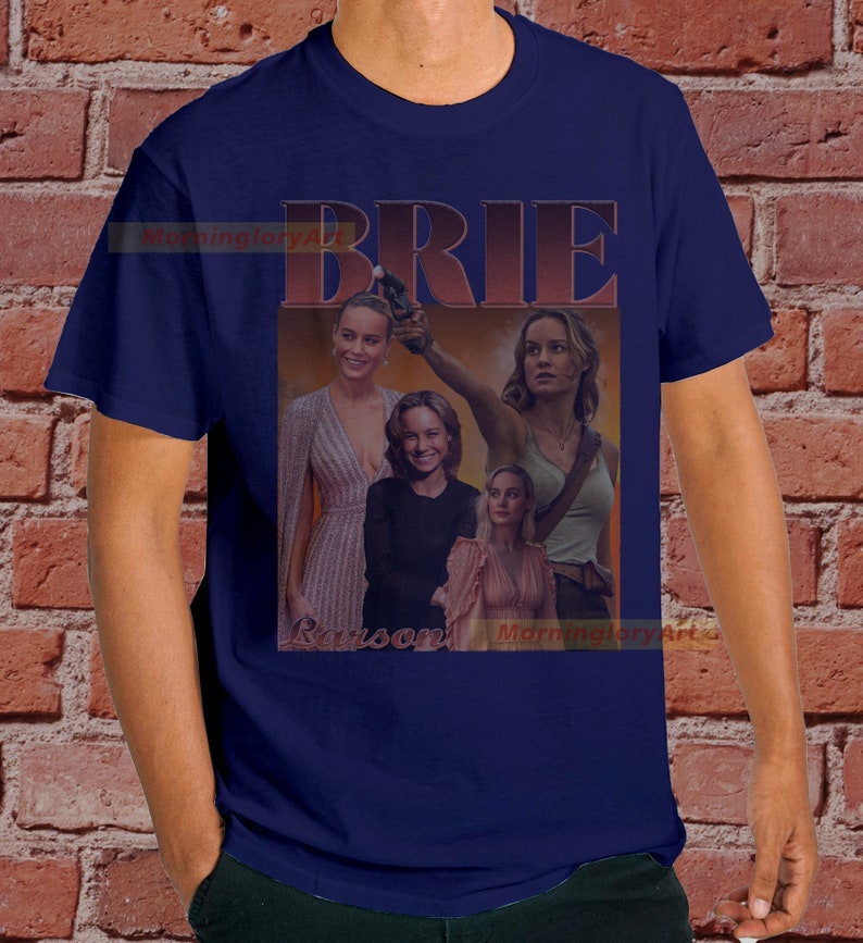 May include: A navy blue t-shirt with a collage of images of Brie Larson. The images are in a retro style with a red and orange color scheme. The text "BRIE" is printed in large, bold letters above the images.