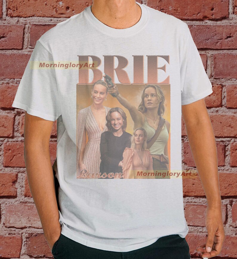 May include: White t-shirt with a collage of images of Brie Larson. The images are in a retro style with a faded, vintage look. The text "BRIE" is printed in large, bold letters across the top of the shirt.