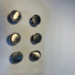 May include: Six silver-toned cabinet knobs with a decorative, octagonal design. The knobs are arranged in two rows of three.