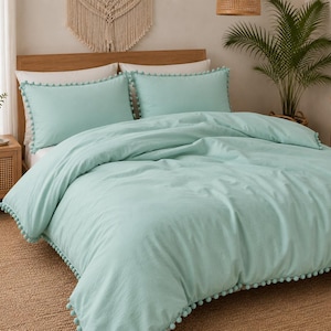 Può includere: Un set copripiumino color verde menta chiaro che include due federe abbinate. Il copripiumino e le federe sono decorati con un bordo di piccoli pon pon rotondi. Il tessuto presenta un aspetto leggermente testurizzato in un colore solido.