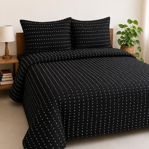 May include: A black quilt and two matching pillow shams featuring a vertical pattern of small, white dashed lines. The bedding set has a quilted texture with a consistent grid-like stitch pattern across the fabric surface, providing a uniform look.