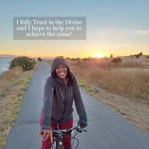 May include: A person wearing a gray hooded sweatshirt rides a bicycle on a paved path. The path is lined with grass and trees. The sky is a vibrant orange and pink as the sun sets in the distance. The text "I fully Trust in the Divine and I hope to help you to achieve the same!" is displayed at the top of the image.