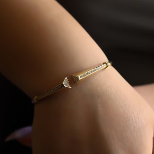 May include: A gold bangle bracelet with a pointed design and small clear stones.