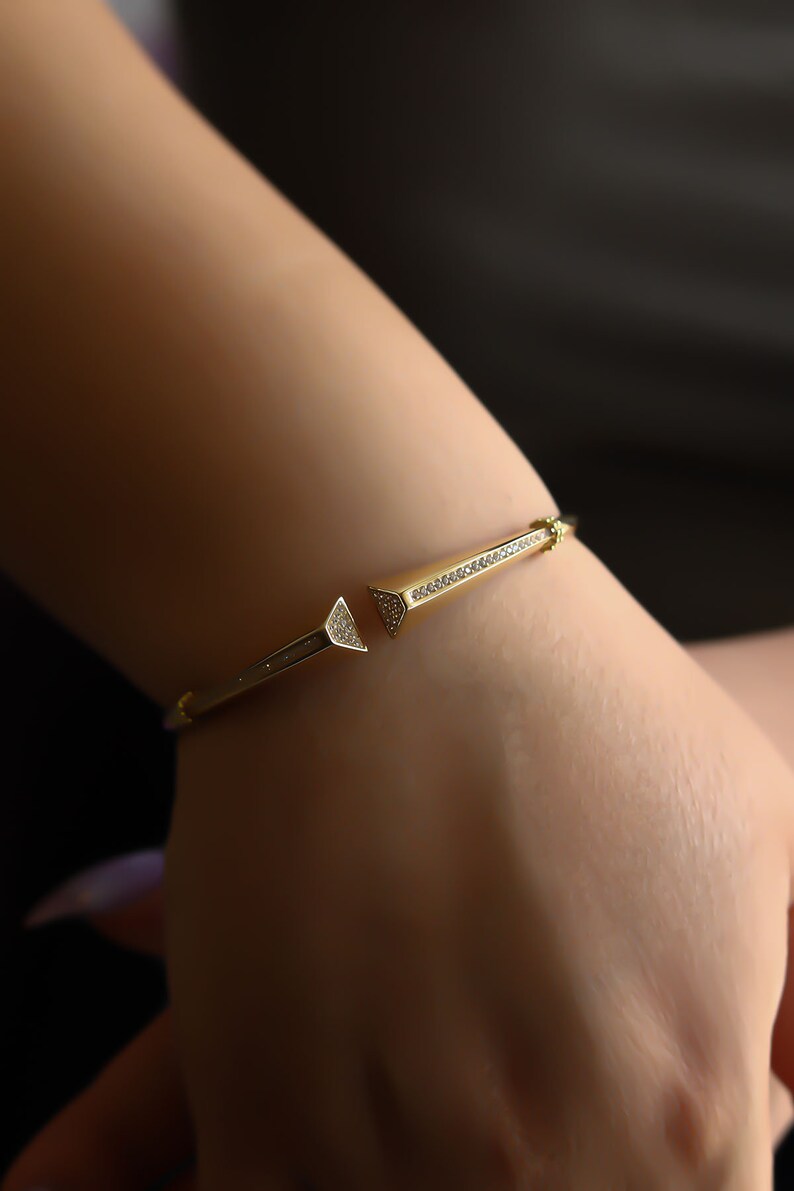 May include: A gold bangle bracelet with a pointed design and small clear stones.