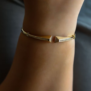 May include: A gold bracelet with a geometric design. The bracelet is set with small, clear stones.