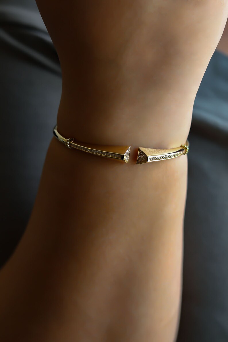 May include: A gold bracelet with a geometric design. The bracelet is set with small, clear stones.