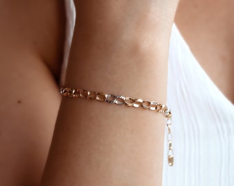 May include: A gold chain bracelet with a textured design. The bracelet is on a person's wrist.