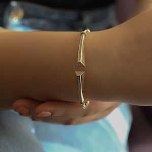 May include: A gold bangle bracelet with a diamond-like design. The bracelet has two triangular ends that point towards each other.