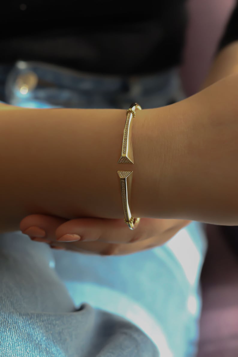 May include: A gold bangle bracelet with a diamond-like design. The bracelet has two triangular ends that point towards each other.