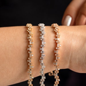 May include: Three gold, silver, and rose gold bracelets with baguette-shaped diamonds. The bracelets are stacked on a person's wrist.