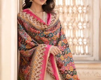 May include: A vibrant shawl with a pink border and detailed floral designs. The shawl displays a range of colours, including pink, blue, yellow, and orange. The garment is draped over the shoulders.