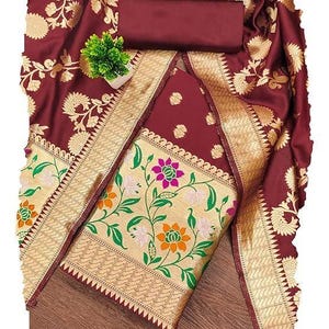 May include: A deep maroon fabric set featuring intricate gold floral patterns and a wide border. The textile displays a central panel with colourful pink, orange, and white flower motifs on a gold background, complemented by a solid maroon piece.