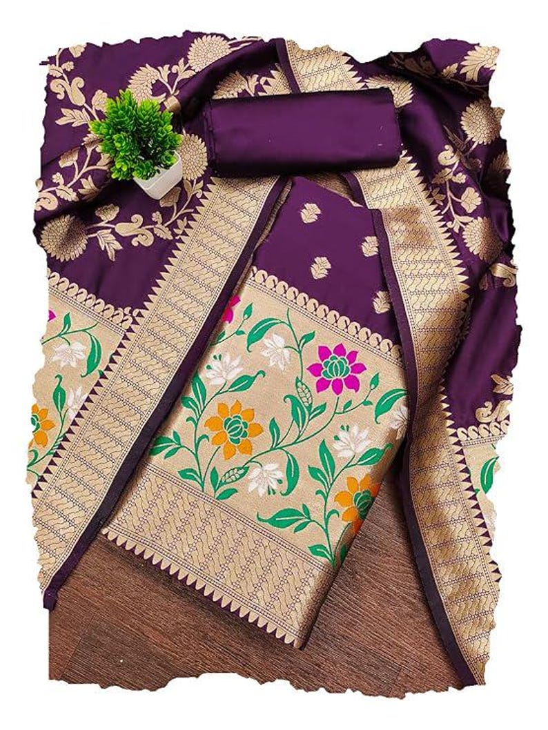 May include: A deep purple fabric with a wide gold border featuring a floral pattern in green, white, orange, and pink. The fabric has a smooth texture and includes a rolled piece of matching purple material and a small green artificial plant.