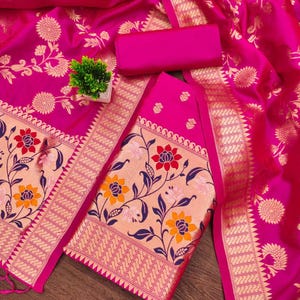 May include: A vibrant fuchsia fabric featuring intricate gold floral patterns and a wide border with detailed botanical motifs in red, orange, and dark blue. The textile includes a matching solid fuchsia rectangular piece and a small green plant.
