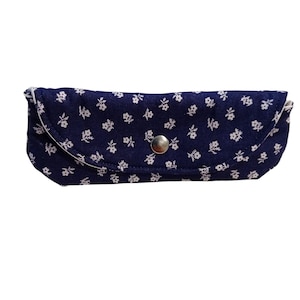 Può includere: Un astuccio per occhiali blu navy con un motivo floreale bianco. L'astuccio è rettangolare con una parte superiore curva e una chiusura a scatto argentata. L'interno è foderato in tessuto bianco.