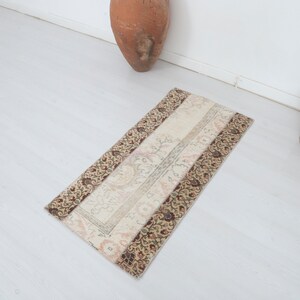 May include: A rectangular rug with a white center and a brown and beige patterned border. The rug is on a white floor.
