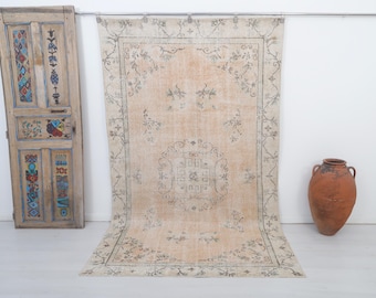 Puede incluir: Una alfombra vintage con fondo beige claro y un patrón floral descolorido. La alfombra tiene un borde decorativo con un diseño gris claro y blanco.