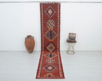May include: A long, red runner rug with a geometric pattern in shades of brown, black, and white. The rug has a fringe on both ends.
