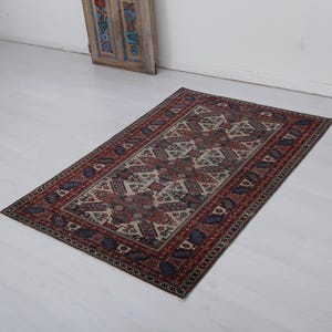 May include: A vintage rug with a cream background and a geometric pattern in shades of red, blue, and black.
