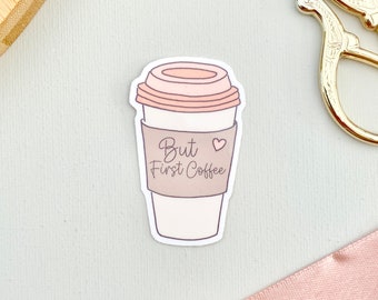 Puede incluir: Una taza de café blanca con una manga de papel marrón que dice "But First Coffee" con un corazón rosa. La taza tiene una tapa rosa con un contorno marrón.