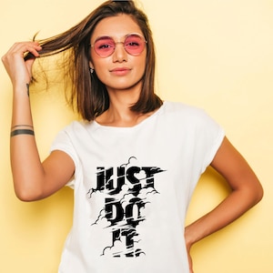 May include: White t-shirt with the text "JUST DO IT" in a black cloud design. The model is wearing pink-tinted sunglasses and has brown hair. The background is a solid yellow color.