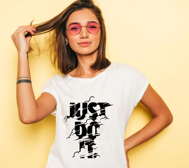 May include: White t-shirt with the text "JUST DO IT" in a black cloud design. The model is wearing pink-tinted sunglasses and has brown hair. The background is a solid yellow color.