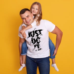 May include: A man wearing a white t-shirt with the text "JUST DO IT" in black, carrying a young girl on his back. Both are wearing blue jeans and white socks. The background is a solid yellow.