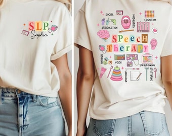 May include: Cream-colored t-shirt with the text "SLP Sophia" on the front, featuring colorful graphics. The back of the shirt displays "Speech Therapy" with related icons. The shirt is paired with denim shorts.