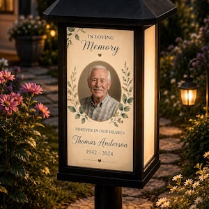 Peut inclure: Une lanterne commémorative solaire noire avec le portrait d'un homme âgé. Le texte indique IN LOVING Memory, FOREVER IN OUR HEARTS, Thomas Anderson et 1942-2024. Le design présente des illustrations de feuilles vertes et des petits cœurs.
