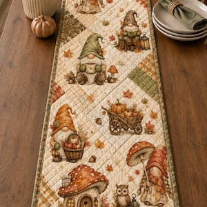 Puede incluir: Un camino de mesa acolchado rectangular con un diseño de patchwork en tonos crema, naranja y verde. La tela está decorada con ilustraciones de gnomos, calabazas, setas y hojas de otoño, rematado con un borde de tela de color verde.